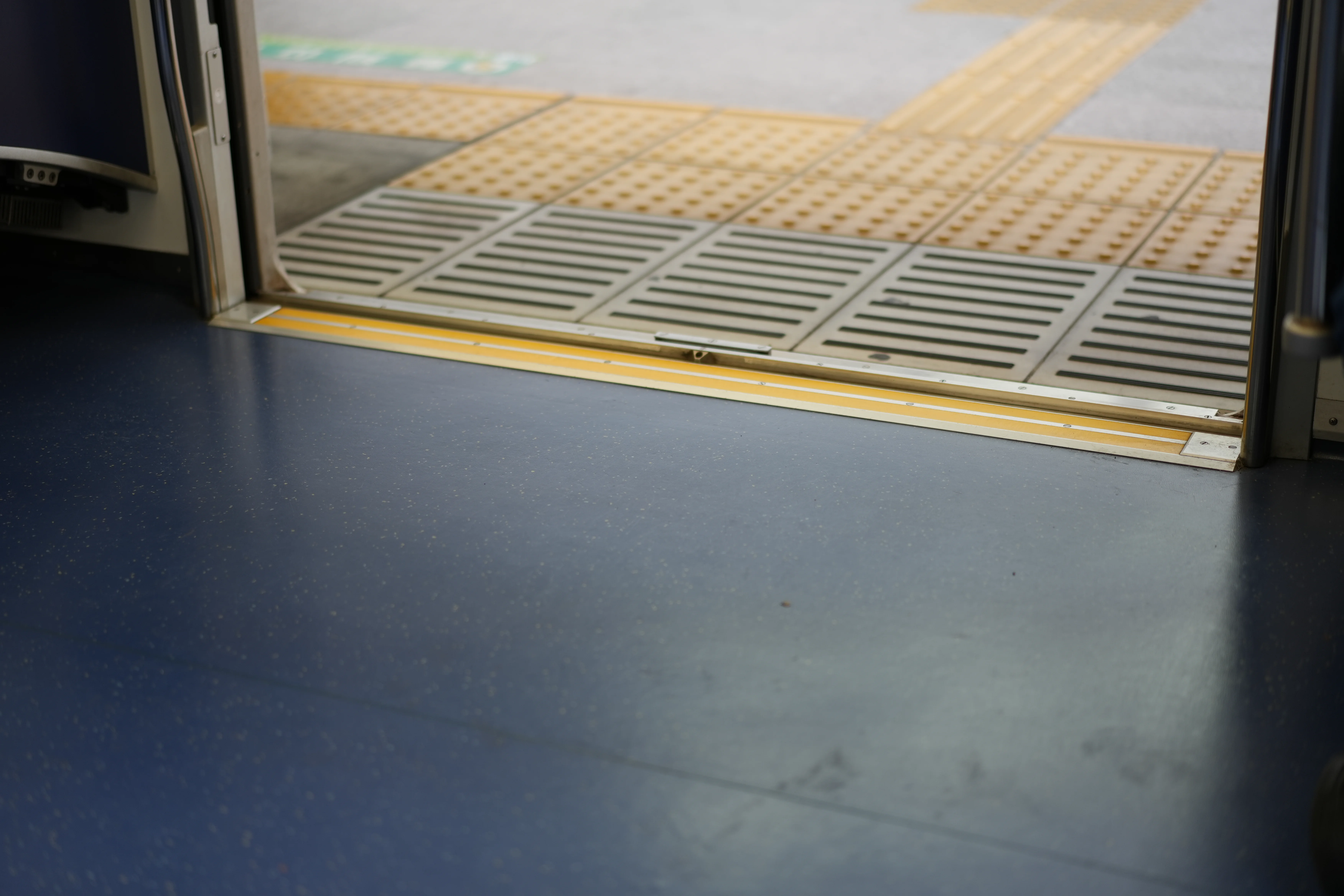 Light falls across a metal threshold, textured paving, and a dark floor.
